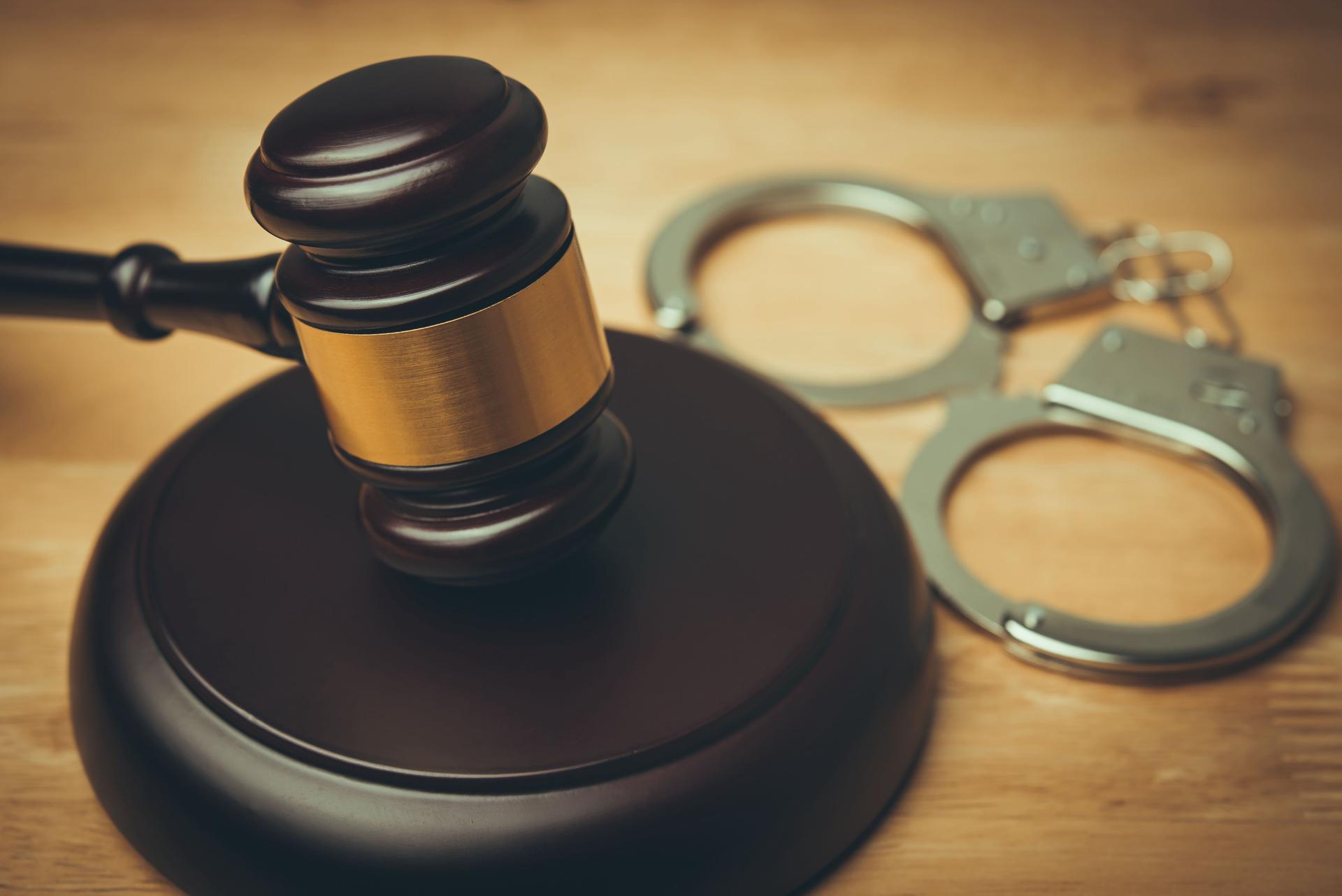 Hammer judge gavel and handcuffs in courtroom on wooden table background.